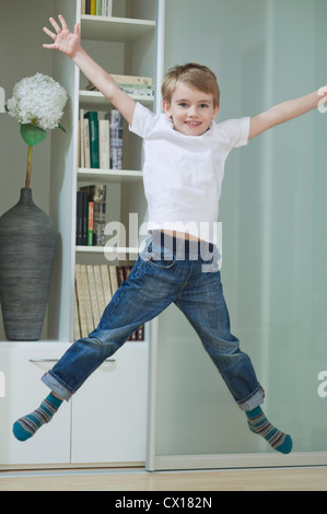 Ritratto di un ragazzo in casuals jumping in mid-aria di casa Foto Stock