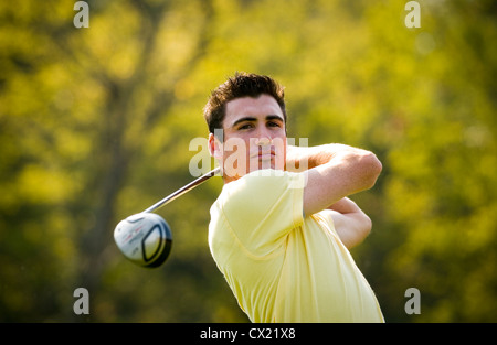 Un golfista maschio in una maglietta gialla completa il suo swing con un autista. Foto Stock