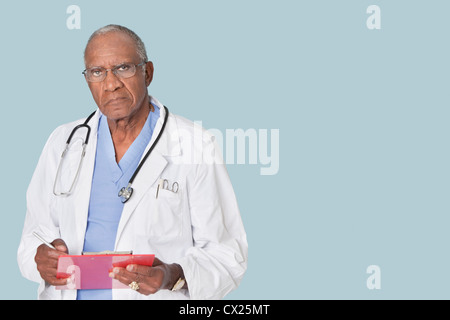 Ritratto di un americano africano senior medico tenendo appunti su fondo azzurro Foto Stock