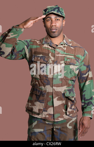 Ritratto di un giovane americano africano US Marine Corps soldato salutando su sfondo marrone Foto Stock
