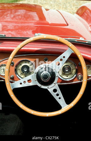 Un volante in legno, scudo auto e interno del rosso auto d'epoca con tetto basso Foto Stock