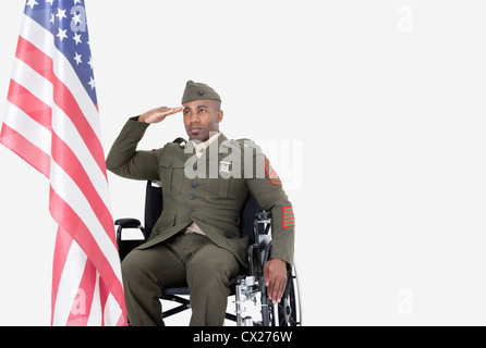 Giovane soldato americano in sedia a rotelle salutando bandiera americana su sfondo grigio Foto Stock