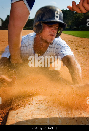 Un casco che indossa college giocatore di baseball scorre in terza base su un campo scuola Foto Stock