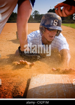 Un casco che indossa college giocatore di baseball scorre in terza base su un campo scuola Foto Stock