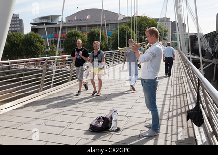 Busker suonare la tromba sul Giubileo d oro ponte pedonale sul Tamigi da Hungerford Bridge Foto Stock