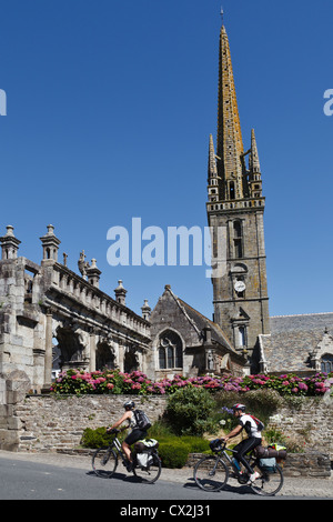 I ciclisti passando davanti alla chiesa di Saint Suliau e il XVI secolo arco trionfale, Sizun, Finistère Bretagna, Francia Foto Stock