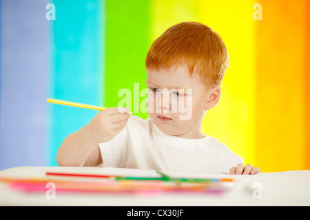 Redheaded ragazzo adorabile disegno con matita gialla su sfondo arcobaleno Foto Stock