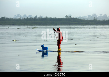 Un uomo vestito con un costume da supereroe pagaie di stand up paddle board (SUP) con gomma mucca giocattolo sul fiume Kampar in Sumatra. Foto Stock