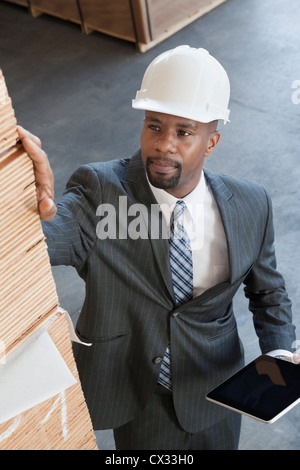 Elevato angolo di vista americano africano contraente maschio ispezione di tavole di legno mentre si tiene un tablet PC Foto Stock