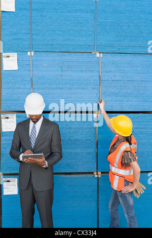 African American maschio di ingegnere di lavoro su tablet PC mentre femmina lavoratore industriale Controllo assi in legno Foto Stock