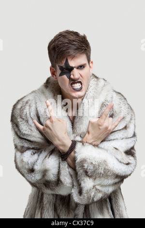 Ritratto di giovane frustrato uomo in pelliccia denti di aggraffaggio e rendendo il gesto ribelle contro lo sfondo grigio Foto Stock
