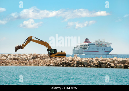 La costruzione di una diga. Escavatore pietre messe in mare. Una nave sullo sfondo Foto Stock