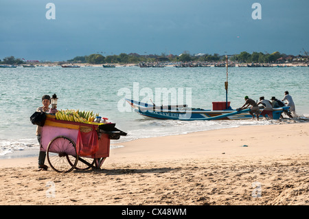 Barche da pesca e di tutoli di mais venditore sulla spiaggia di Jimbaran, Bukit penisola meridionale di Bali, Indonesia. Foto Stock