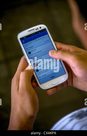 Un telefono intelligente utente accede a Facebook su Internet. Foto Stock