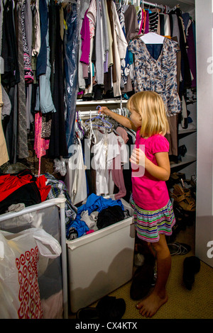 Contribuendo con mansioni domestiche, una bambina di sette anni pende vestiti in sua madre armadio a casa a Lake Forest, CA. Foto Stock