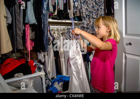 Contribuendo con mansioni domestiche, una bambina di sette anni pende vestiti in sua madre armadio a casa a Lake Forest, CA. Foto Stock