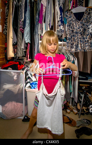 Contribuendo con mansioni domestiche, una bambina di sette anni pende vestiti in sua madre armadio a casa a Lake Forest, CA. Foto Stock