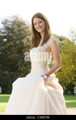 Giovane donna in crema senza spalline abito nuziale holding gonne in motivi di Sede statali Foto Stock