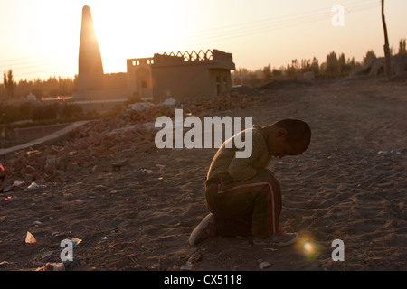 Un giovane ragazzo di Uighur siede nella sporcizia in Turpan, Xinjiang, Cina Foto Stock