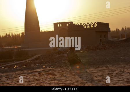 Un giovane ragazzo di Uighur siede nella sporcizia in Turpan, Xinjiang, Cina Foto Stock