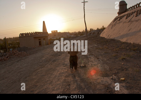 Un giovane ragazzo di Uighur passeggiate lungo una via in Turpan, Xinjiang, Cina Foto Stock