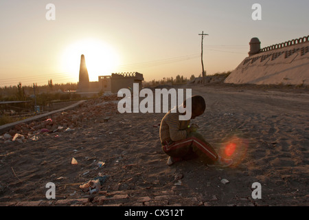 Un giovane ragazzo di Uighur siede nella sporcizia in Turpan, Xinjiang, Cina Foto Stock