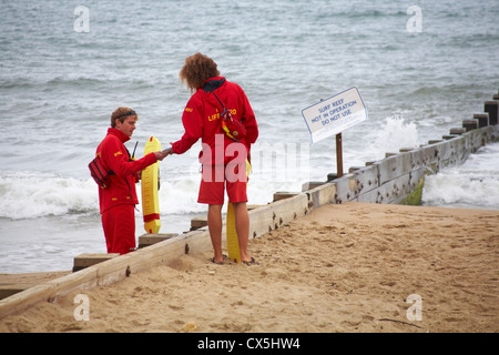 Due maschio RNLI bagnini a Boscombe spiaggia vicino surf reef non è in operazione segno nel mese di agosto Foto Stock