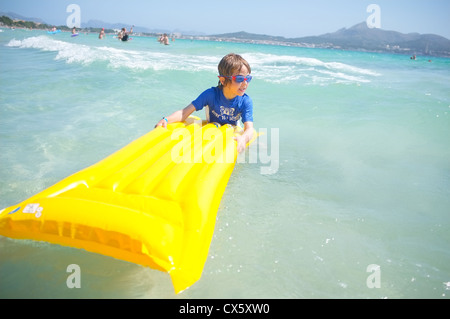 Un giovane ragazzo divertendosi nel surf su una zattera gonfiabile lilo indossando sun top di proiezione Foto Stock