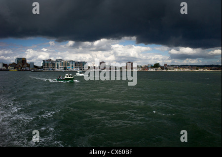 Un meteo Storm nero nube si avvicina oltre il porto di Poole mentre il mare le barche sono inondate di luce solare Foto Stock