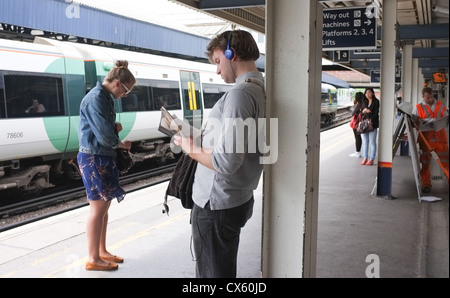 I passeggeri di leggere libri e giornali in attesa su una stazione ferroviaria per il prossimo treno Foto Stock