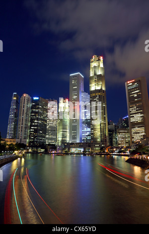 Sentieri di luce delle barche sul Fiume Singapore con alti edifici del centro cittadino di Singapore in background. Foto Stock