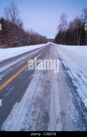 Neve e ghiaccio strada coperta al crepuscolo Foto Stock