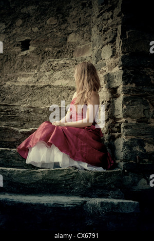 Una ragazza in un abito rosso è seduto sui gradini di pietra Foto Stock