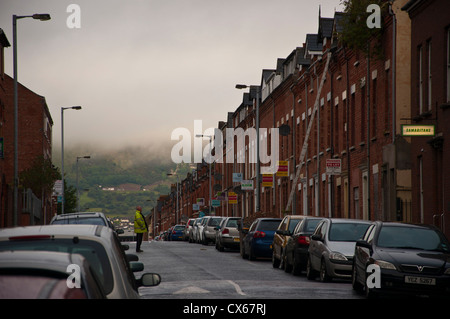 Strada di case a schiera a Belfast con Divis colline dietro Wellseley Ave Foto Stock