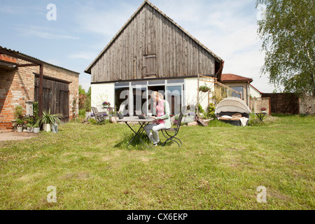 Una donna seduta al tavolo nel suo cortile posteriore utilizzando un computer portatile Foto Stock