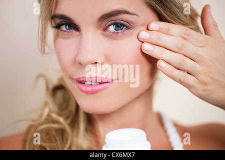 Una giovane donna bionda che l'applicazione di crema idratante per il viso da vicino Foto Stock