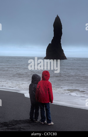 Due bambini sotto la pioggia guardando il Reynisdrangar (mare di basalto pile) in Vik (vik mi myrdal), a sud dell'Islanda Foto Stock