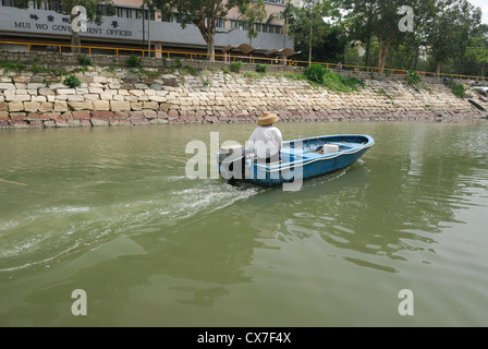Pescatore che viaggiano fino il fiume Silvermine nella sua piccola barca, Mui Wo Cina. Foto Stock