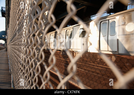 Il treno visto attraverso la recinzione di filo che separa il passaggio pedonale sul ponte di Manhattan Foto Stock