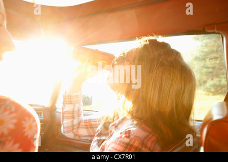 Una donna di bere da un possibile mentre sedendo nel sedile del passeggero di auto d'epoca Foto Stock