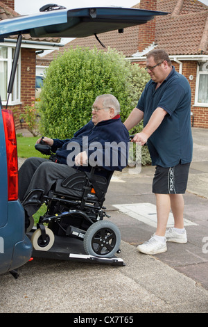 Caregiver maschio figlio spingendo un disabile uomo anziano in una sedia a rotelle su un costruito in rampa in un appositamente auto adattata per ottenere circa Foto Stock