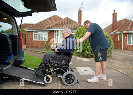 Caregiver maschio figlio spingendo un disabile uomo anziano in una sedia a rotelle su un costruito in rampa in un appositamente auto adattata per ottenere circa Foto Stock