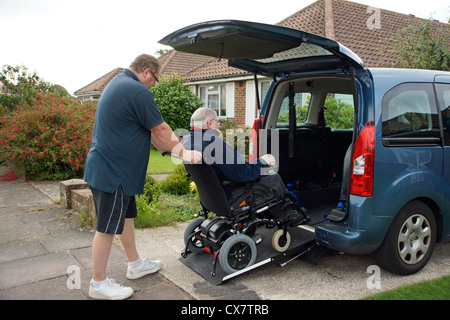 Caregiver maschio figlio spingendo un disabile uomo anziano in una sedia a rotelle su un costruito in rampa in un appositamente auto adattata per ottenere circa Foto Stock