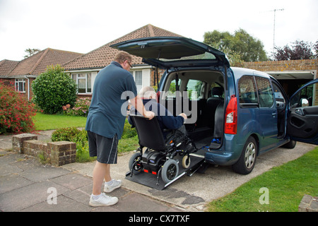 Caregiver maschio figlio spingendo un disabile uomo anziano in una sedia a rotelle su un costruito in rampa in un appositamente auto adattata per ottenere circa Foto Stock