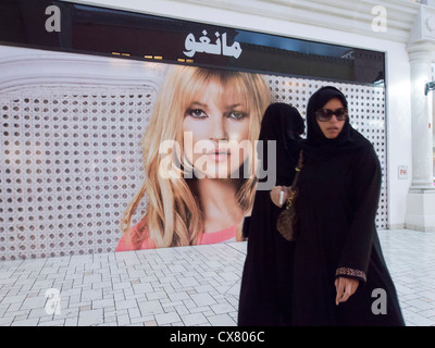 Donne arabe a piedi passato western cartellone su shop nella sistemazione di villaggio shopping mall a Doha in Qatar Foto Stock