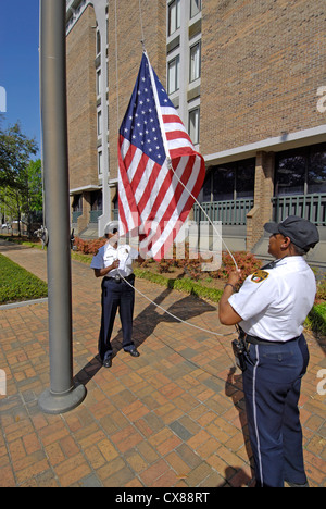 Maschio e femmina neri degli ufficiali di polizia prendere la bandiera Americal giù una piega che alla fine della giornata a Montgomery in Alabama al Foto Stock