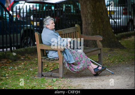 Anziana signora sola seduta su una panchina nel parco in Bath Somerset England Regno Unito Foto Stock