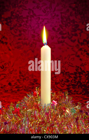 Una festa di Natale candela e scintillante di tinsel su uno sfondo rosso, trattata in una maniera surrealista Foto Stock