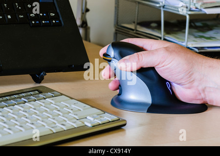 L'uomo utilizza un pinguino ergonomica verticale il mouse del computer per le persone con dolori al polso Foto Stock