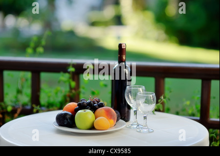 Sul tavolo bianco è una bottiglia di vino con gli occhiali e la frutta matura Foto Stock
